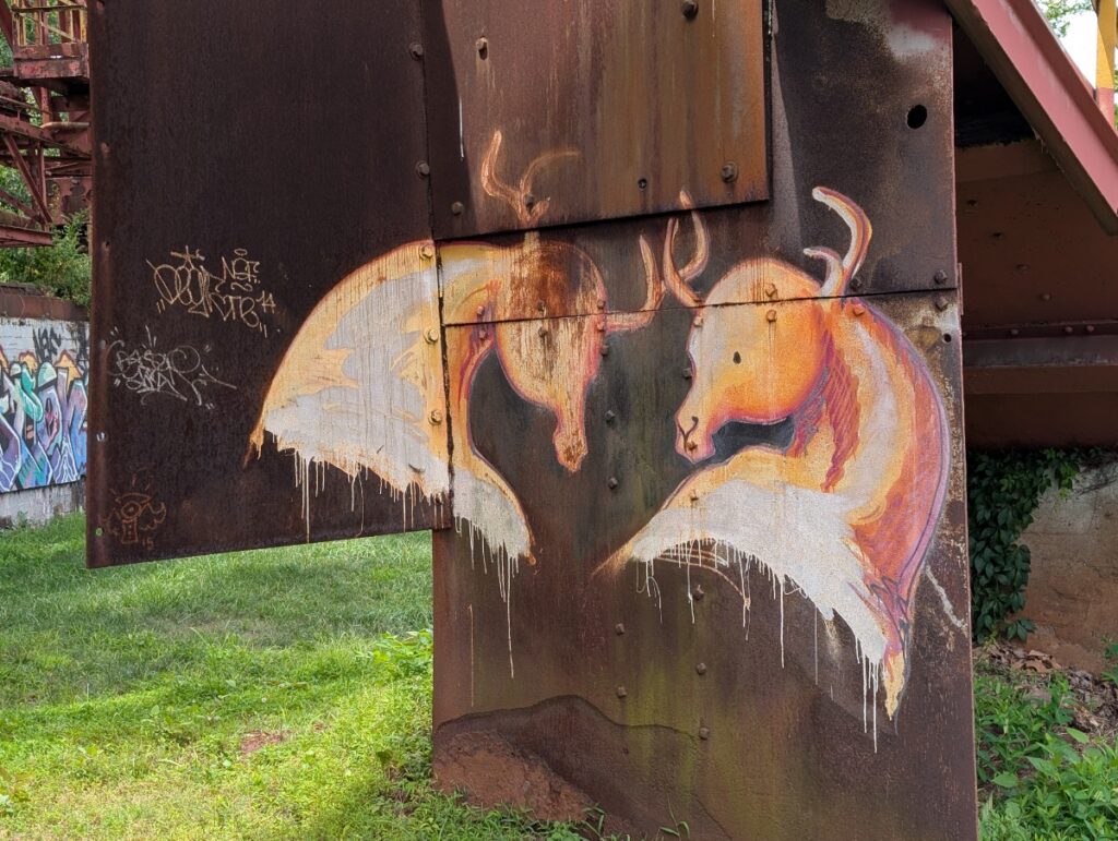 Street art mural of two stylized deer heads painted on a rusted industrial structure at the historic Carrie Furnaces site.