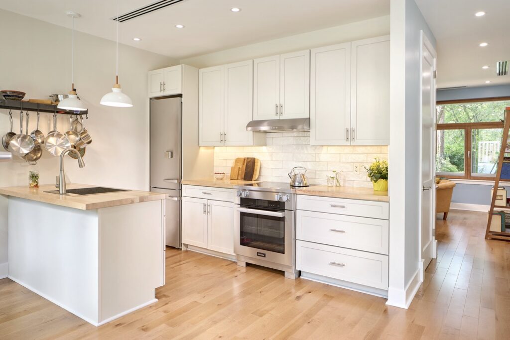 The inside of a home with a white kitchen and stove in between white cabinets.