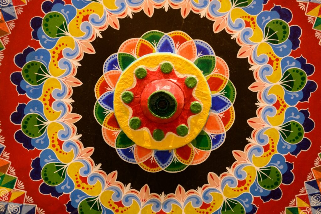 A hand-painted Costa Rican oxcart wheel featuring intricate geometric and floral patterns in red, yellow, and blue.