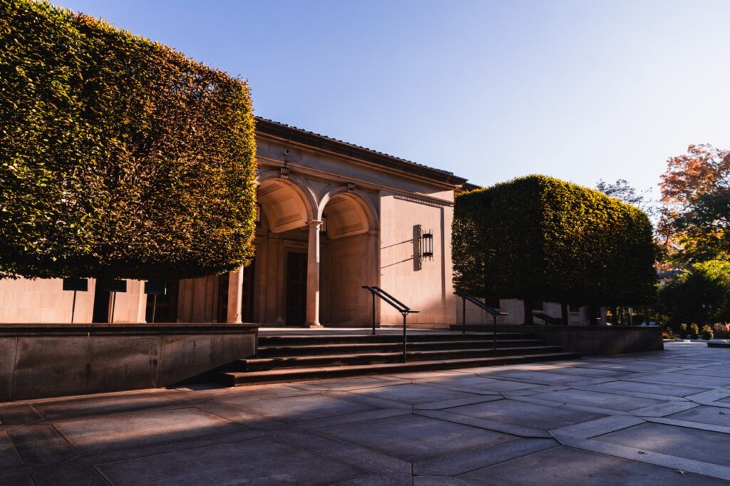 The outside of The Frick Pittsburgh with trees on either side fo the building. 