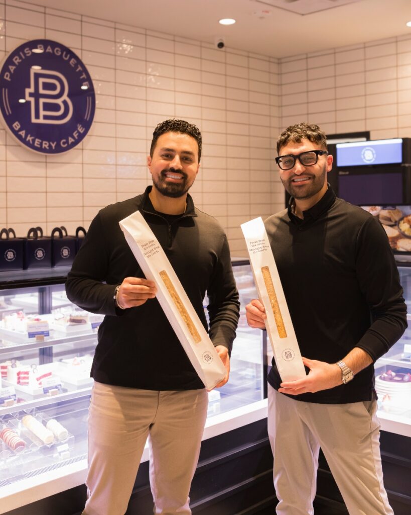 Owners Ali Kamboh and Ammar Zafar holding fresh baguettes inside the Paris Baguette bakery cafe in Shadyside, Pittsburgh.