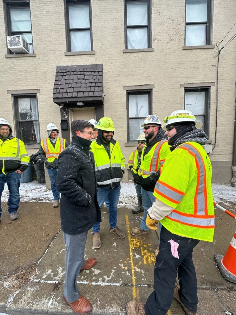Mayor Corey O'Connor speaking with construction workers and contractors on a snowy Pittsburgh street regarding infrastructure and housing projects.