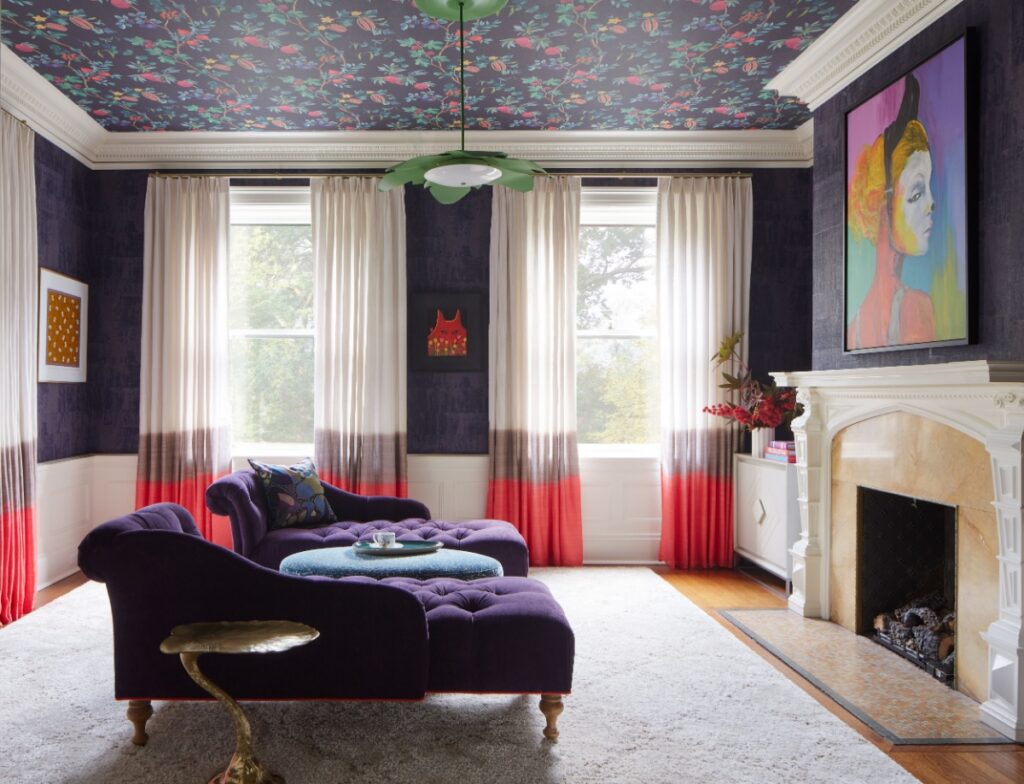 A formal living room with dark walls, a floral-patterned ceiling, and a matching purple velvet chaise lounge and ottoman.