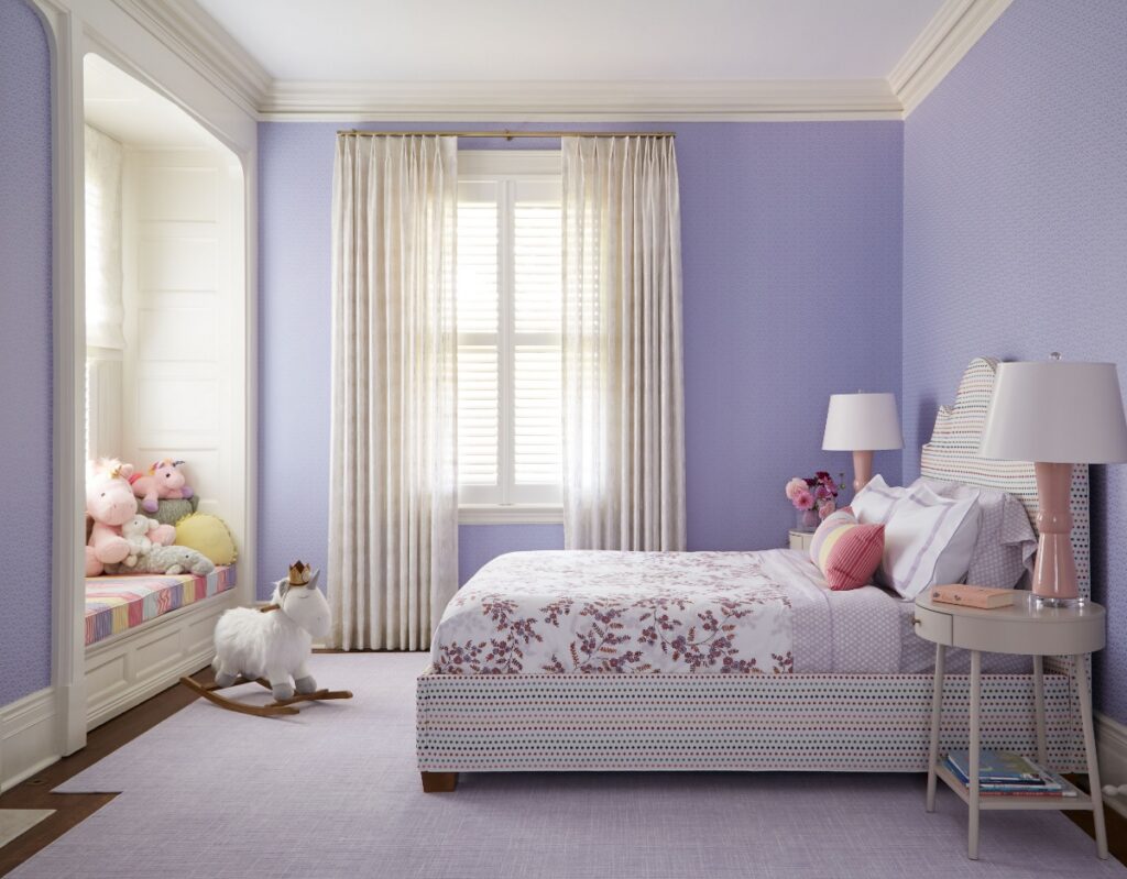 A whimsical purple bedroom designed for a child in a historic Sewickley home, featuring a striped bed with floral bedding, a custom built-in window seat packed with stuffed animals, and a large plush unicorn rocking horse.