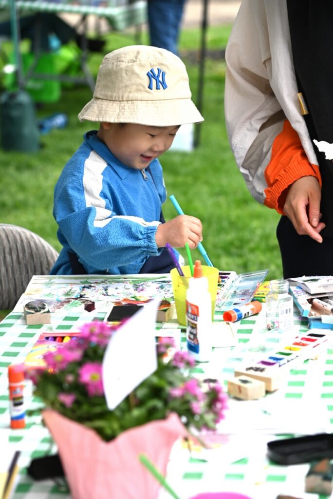 A young child in a bucket hat painting at a craft table during the annual Arbor Day celebration at Mellon Park in Pittsburgh.