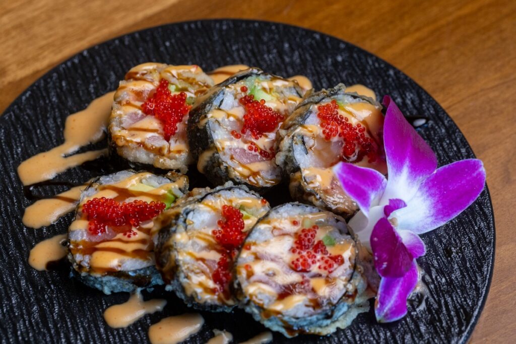 Platter of Godzilla sushi rolls with spicy mayo, eel sauce, and red tobiko garnished with a purple orchid at Otaru.