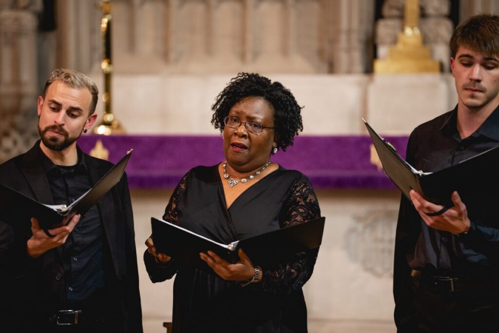 Professional vocalists of the Pittsburgh Camerata performing a contemporary choral arrangement with sheet music.