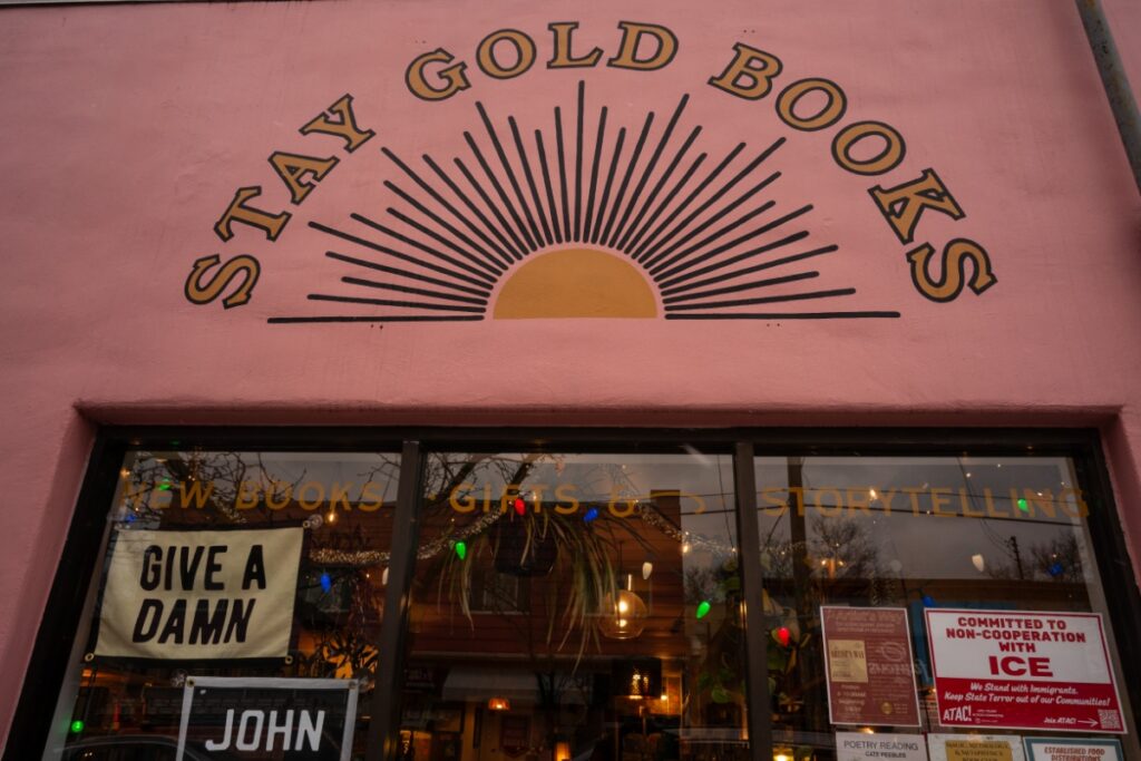 The storefront of Stay Gold Books in Regent Square, featuring a sunburst logo and window signs advocating for community and social causes.