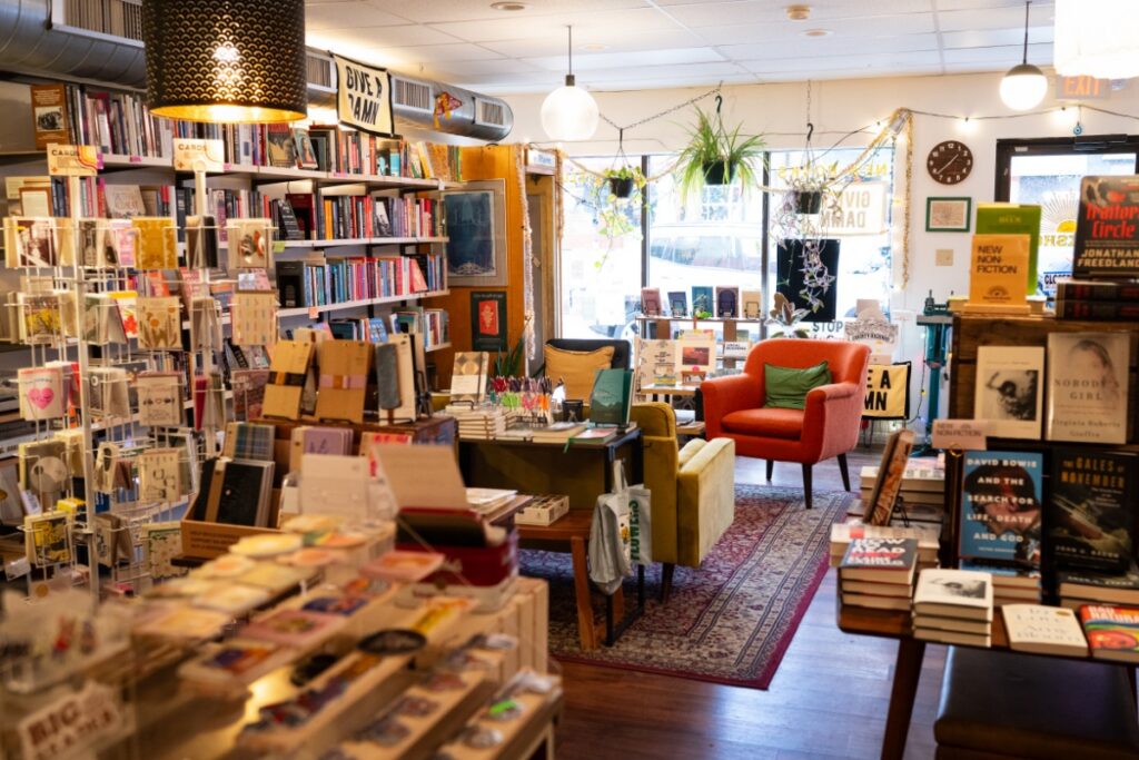 The interior of Stay Gold Books in Regent Square, featuring curated bookshelves, a cozy reading nook with a green armchair, and a local interest section with Pittsburgh-themed gifts.