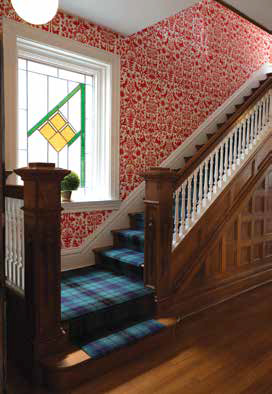 A traditional tartan carpet runner on stairs next to original dark woodwork and whimsical red and white folklore wallpaper.
