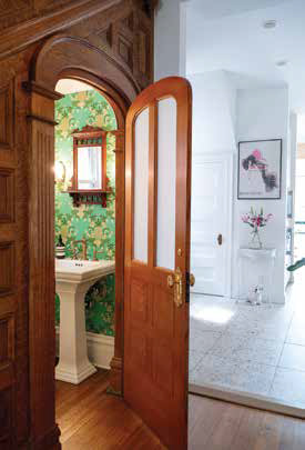An open wooden door leading into a vibrant green and gold patterned powder room with a white pedestal sink.