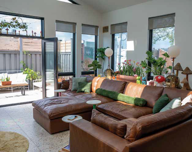 The bright California Room addition featuring a large brown leather sectional sofa, terrazzo tile flooring, and large windows looking onto a patio.
