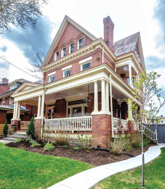 Exterior view of a historic 1899 Queen Anne Victorian home in Highland Park featuring brick siding, a large wrap-around porch, and Romanesque arched windows.
