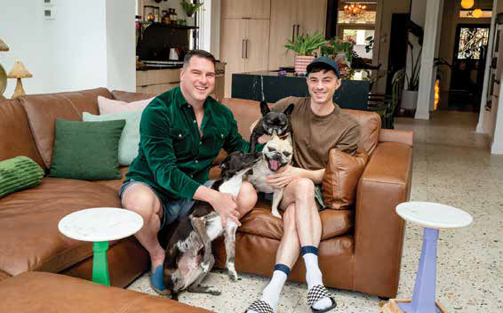 Homeowners Shawn Aversa and Jamie McAdams smiling on a brown leather sectional couch with their pet dogs in their modern living room addition.