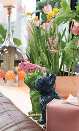 Close-up of glossy green and dark blue ceramic French Bulldog figurines on a window ledge next to fresh pink tulips.