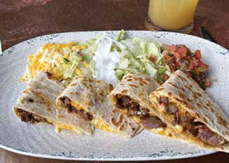 Sliced cheesy steak quesadillas served on a platter with shredded cheese, sour cream, shredded lettuce, and fresh pico de gallo.