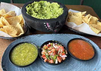 A stone molcajete filled with fresh homemade guacamole served with three varieties of house-made salsa and tortilla chips.