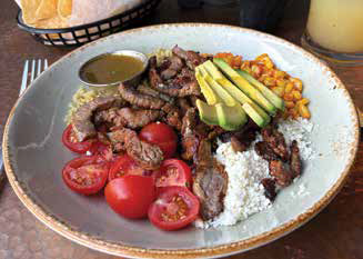 A build-your-own Mexican bowl filled with grilled steak, fresh avocado slices, diced tomatoes, corn, and cotija cheese.