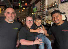 Co-owners Brian Magaritz, Rebecca Avila, and Henry Avila smiling together at the bar with a young child.