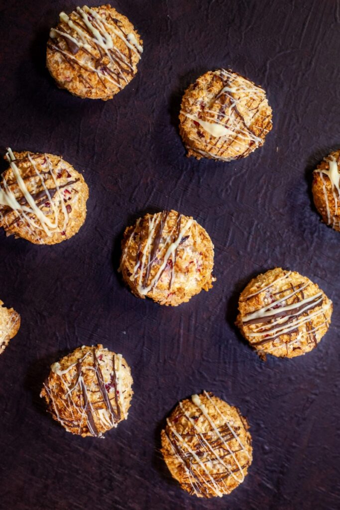 Individual coconut cranberry macaroons sit on a purple tablecloth.