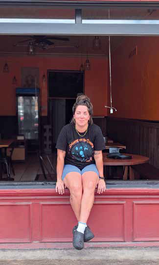 Founder Sarah Coppolo smiling while sitting on the window ledge outside her brick-and-mortar storefront café, Brothmonger, in Bloomfield.