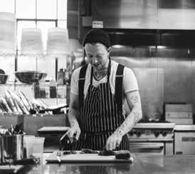 Chef Nik Forsberg in a striped apron preparing food at a stainless steel kitchen counter in his commercial restaurant kitchen.