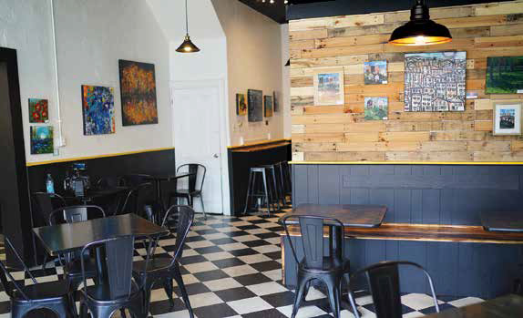 The interior dining room of The Brinery in Sharpsburg featuring black and white checkered floors, black metal chairs, and a rustic wood paneled accent wall with framed art.