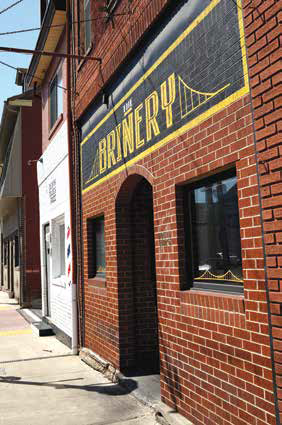 Exterior brick storefront of The Brinery on Main Street in Sharpsburg with an arched entryway and a large black and yellow painted sign.