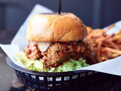 The Graceland sandwich, a crispy fried chicken sandwich with lettuce, pickles, and sauce on a brioche bun, served with a side of french fries in a black basket.