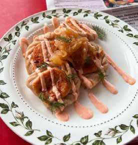 A plate of traditional Polish pierogi topped with caramelized onions, fresh dill, and a creamy pink sauce drizzle on a floral patterned plate.