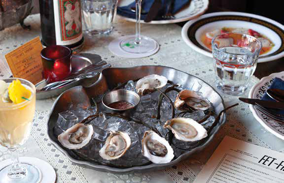 A fresh raw oyster platter served over crushed ice with mignonette sauce on a table at Fet-Fisk restaurant.