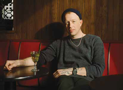 Chef Nik Forsberg wearing a beanie and sitting in a dimly lit red booth at his Bloomfield restaurant, Fet-Fisk.