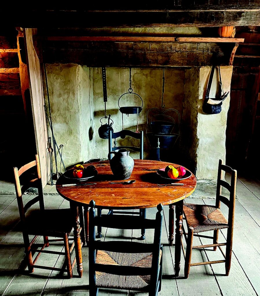 Restored 18th-century interior of the Neill Log House featuring a wooden dining table, period-appropriate chairs, and a hearth with cast-iron cooking pots.