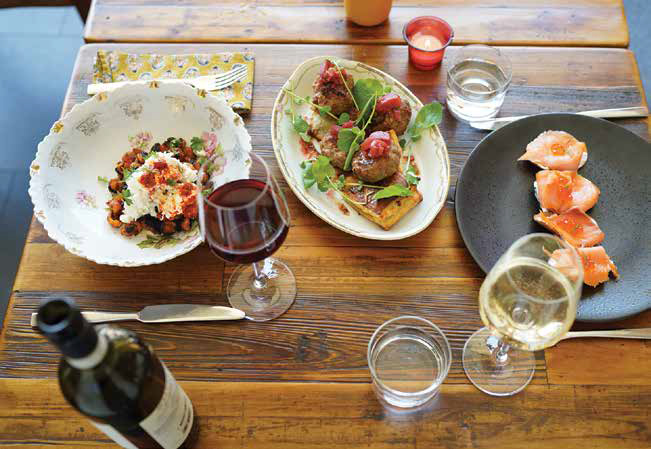 An overhead view of Mediterranean dishes including burrata, meatballs, and salmon roe appetizers served with wine on a wooden table.