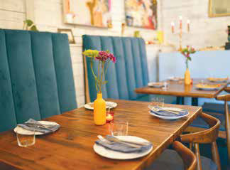 Cozy wooden dining tables with blue velvet banquettes, mismatched plates, and small flower vases inside Senza restaurant.