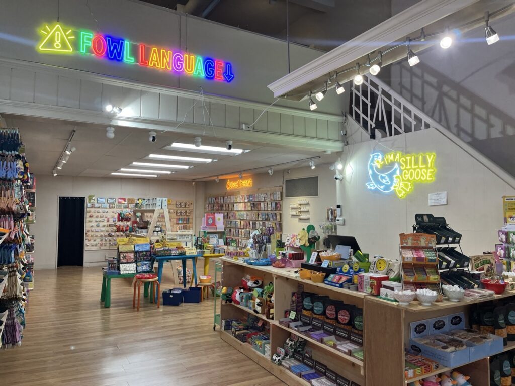 The inside of a store with a counter full of gift items and a neon sign above it. 