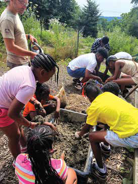 A group of youth participants mixed with mentors working together with soil in a large tray during a summer gardening agriculture workshop.