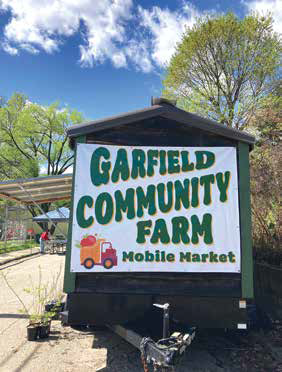 A wooden trailer displaying a large banner for the Garfield Community Farm Mobile Market under a blue sky.