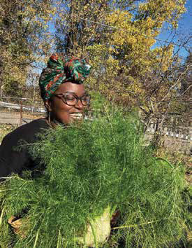 A smiling woman wearing glasses and a colorful headwrap holding a massive bunch of freshly harvested green fennel fronds.