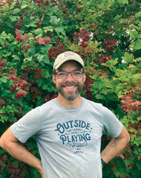 Portrait of John Creasy, executive director of Garfield Community Farm, smiling in front of lush green bushes with red berries.