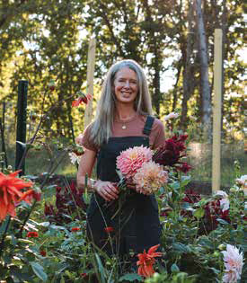 Becca Ringham Myerburg smiling while holding a freshly cut bouquet of pink and burgundy dahlias in a flower field at Eleven Mile Farm.