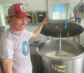 Will Loevner smiling while opening the lid of a large stainless steel pasteurization tank filled with fresh milk at Goat Rodeo creamery.