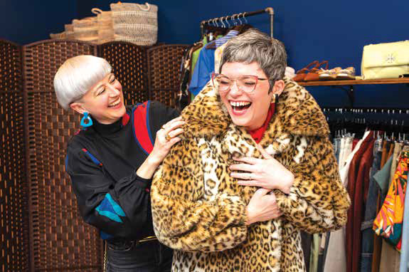 Wardrobe stylist Rachel Vallozzi laughing while helping a client try on a luxury leopard print faux fur coat during a personal styling session.