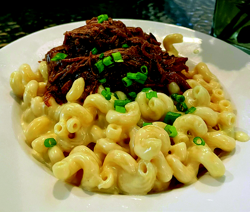 The signature Guinness pot roast mac and cheese at The Woods House, featuring slow-roasted chuck roast over white cheddar cavatappi pasta.
