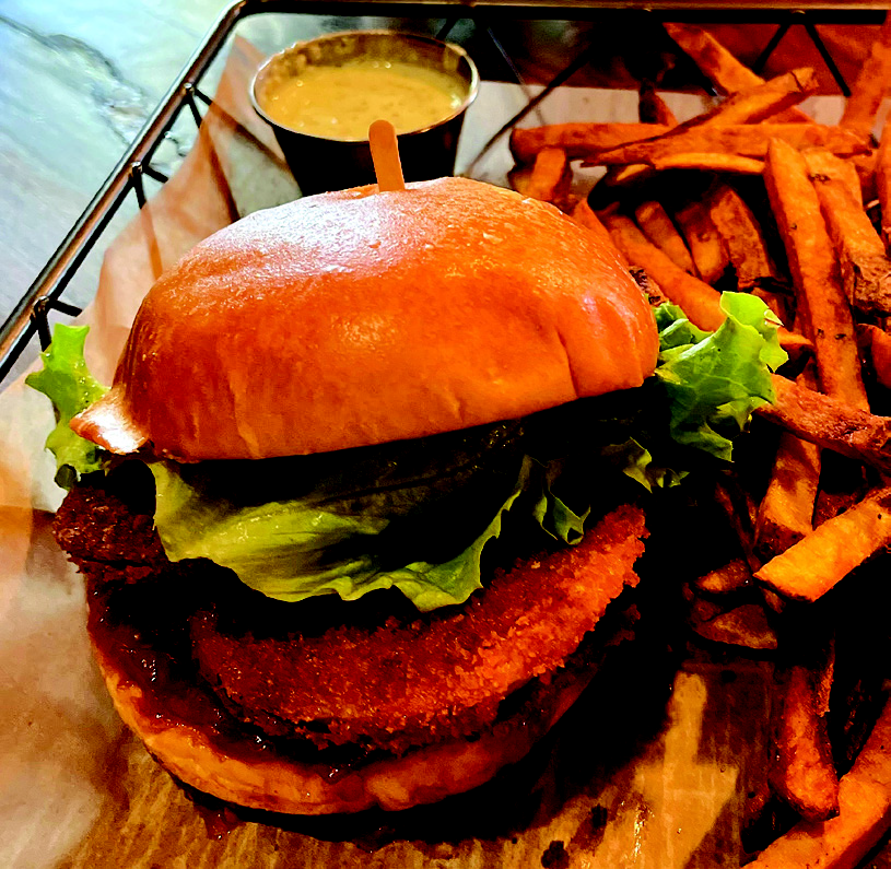 A fried green tomato sandwich with Indian spices served with a side of crispy fries and dipping sauce at The Woods House.
