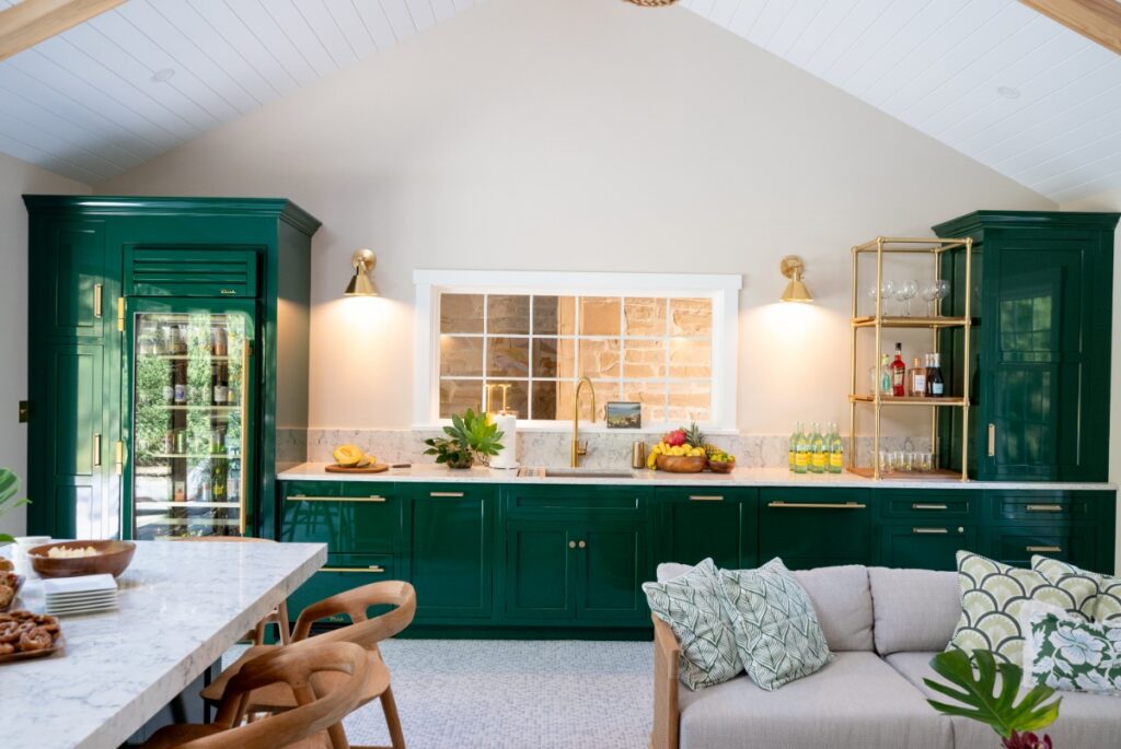 Modern pool house interior featuring custom deep emerald green cabinets, gold sconces, and an open layout.