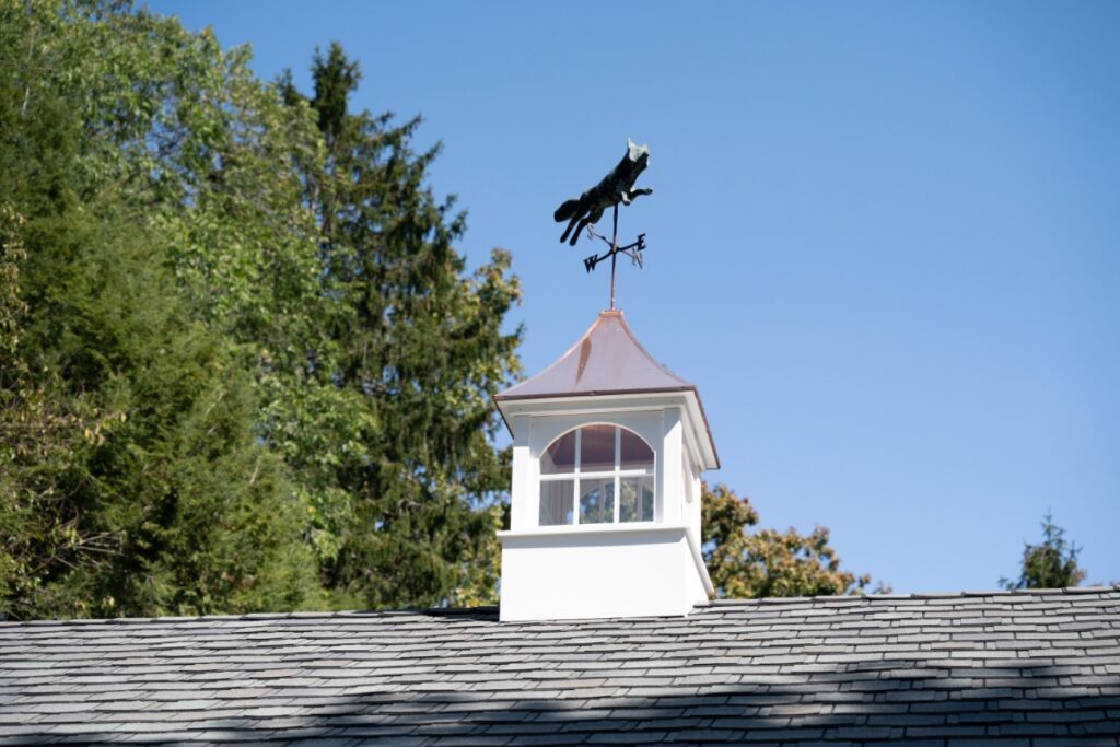 A classic white cupola featuring a jumping fox weather vane on a shingle roof in Fox Chapel.