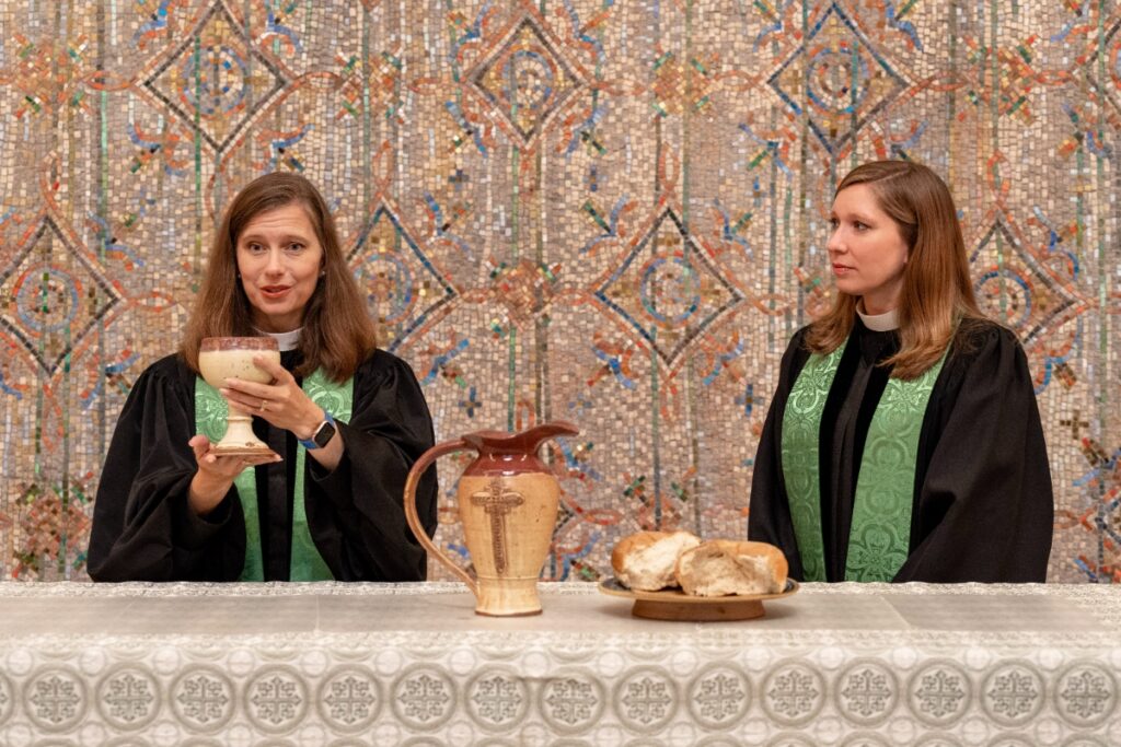 Rev. Austin Shelley holding a communion chalice at the altar with a mosaic background.