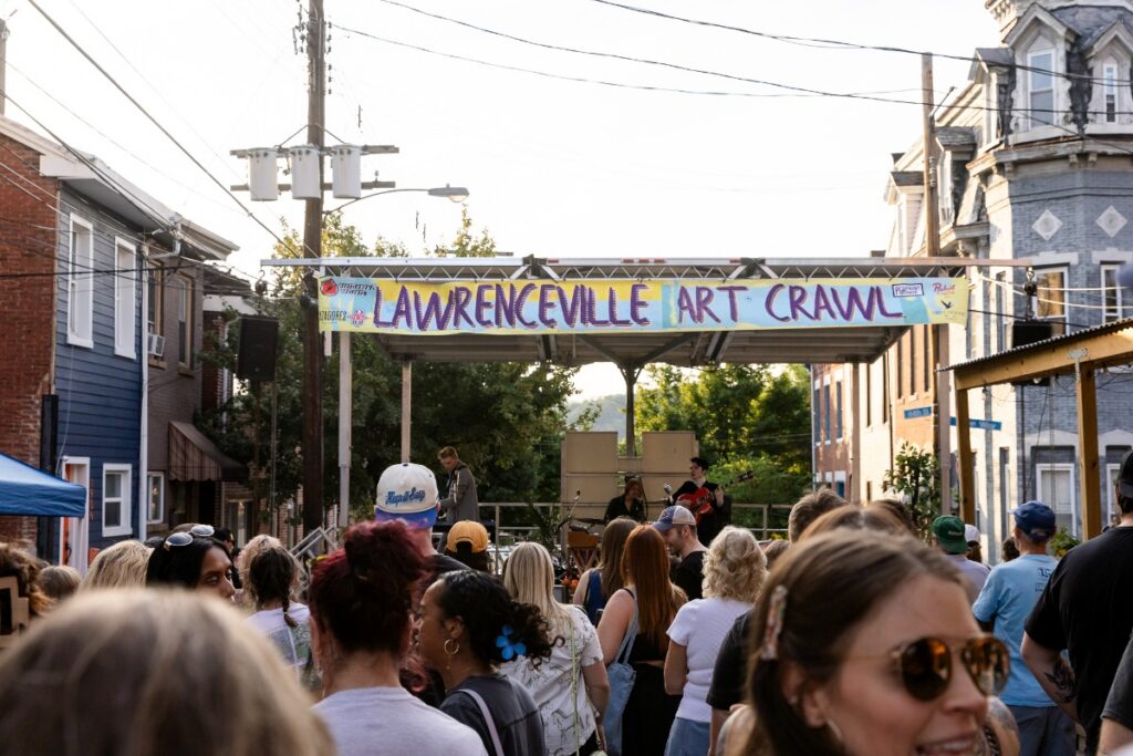 Crowds of visitors walking past outdoor artist booths and local vendor tents on Butler Street during the Lawrenceville Art Crawl in Pittsburgh.