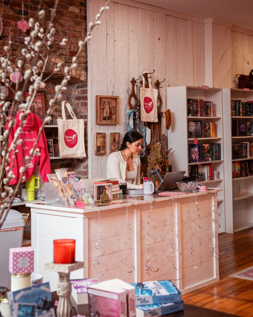 A cozy reading nook with a pink velvet armchair and white bookshelves at Passionate Pages romance bookstore in Lawrenceville.